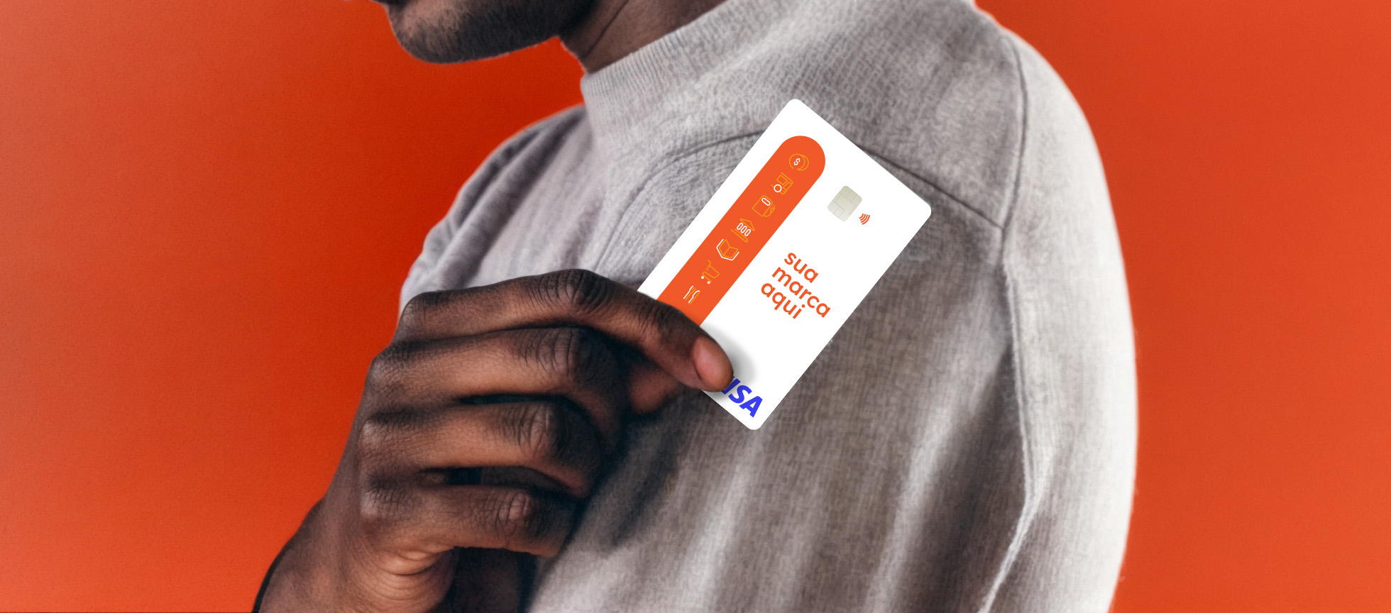 Vemos o ombro de um homem negro de camisa clara, com sua mão direita, em primeiro, plano, segurando um cartão branco e laranja.